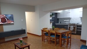 Eine moderne Küche mit Einbauofen, einem Essbereich mit Holztisch und -stühlen sowie einem wandmontierten Flachbildfernseher.