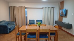 Ein Essbereich mit Holztisch und Stühlen, einem blauen Sofa und einem an der Wand befestigten Fernseher.