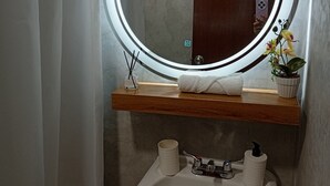 Ein Badezimmer mit rundem Spiegel, Holzablage, Waschbecken und einer Topfpflanze.