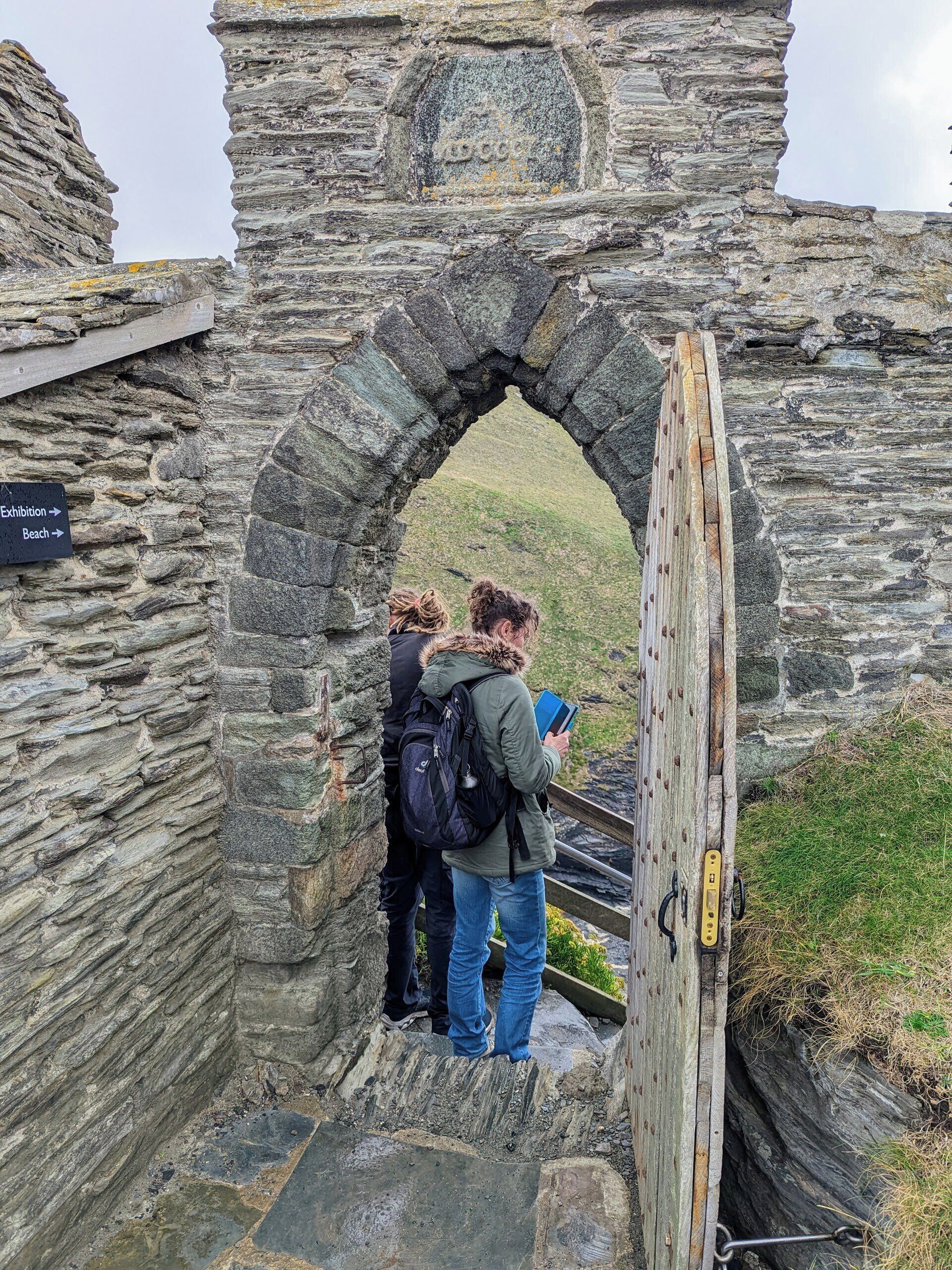 A stone archway leading to a grassy area with a sign indicating directions to the Exhibition and Beach.