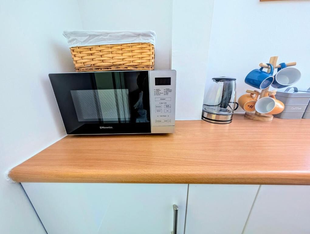 A microwave on a wooden countertop with a basket and a coffee maker.