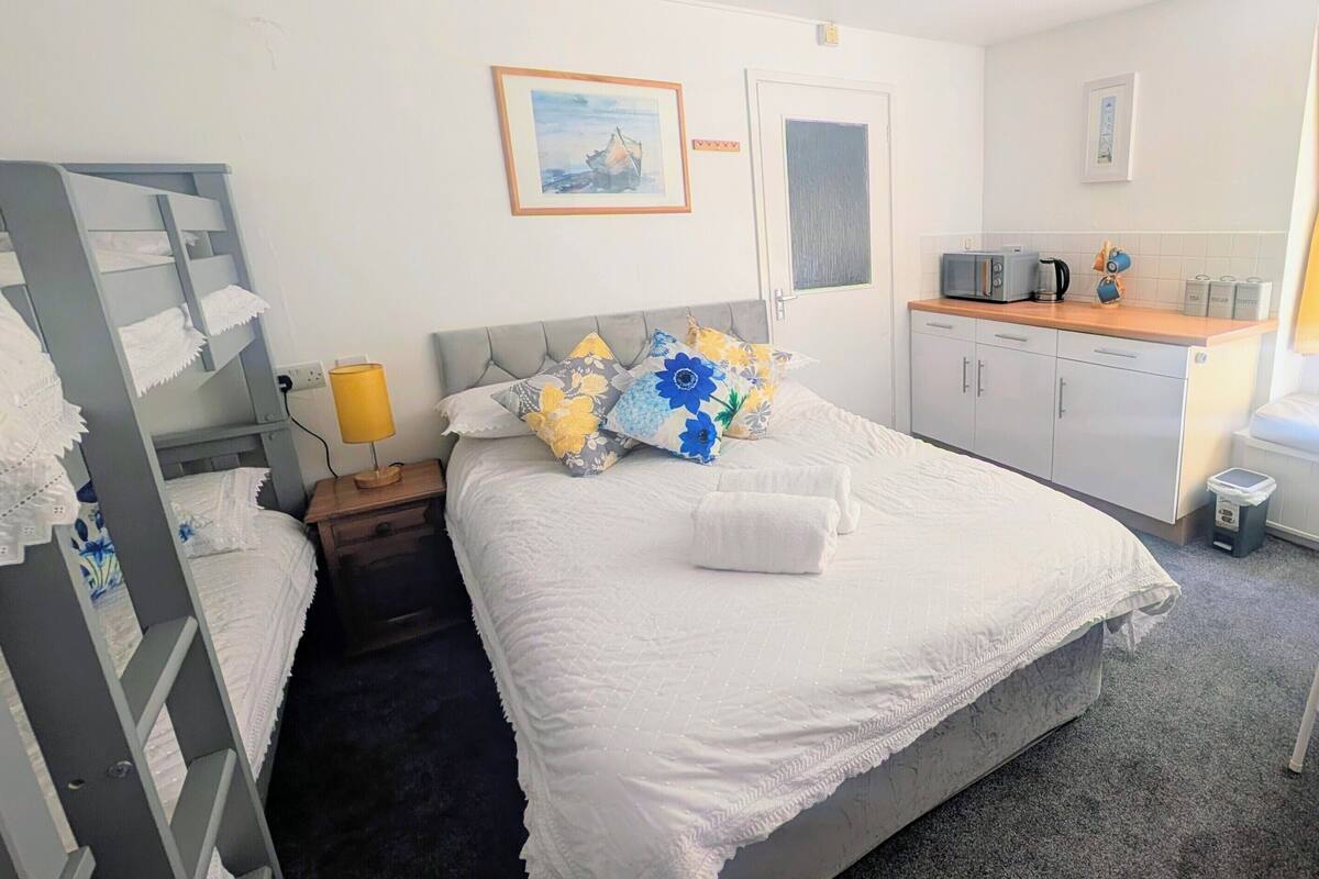 Quarto de hotel com cama, pequeno espaço de cozinha, janela com cortinas e uma cadeira.