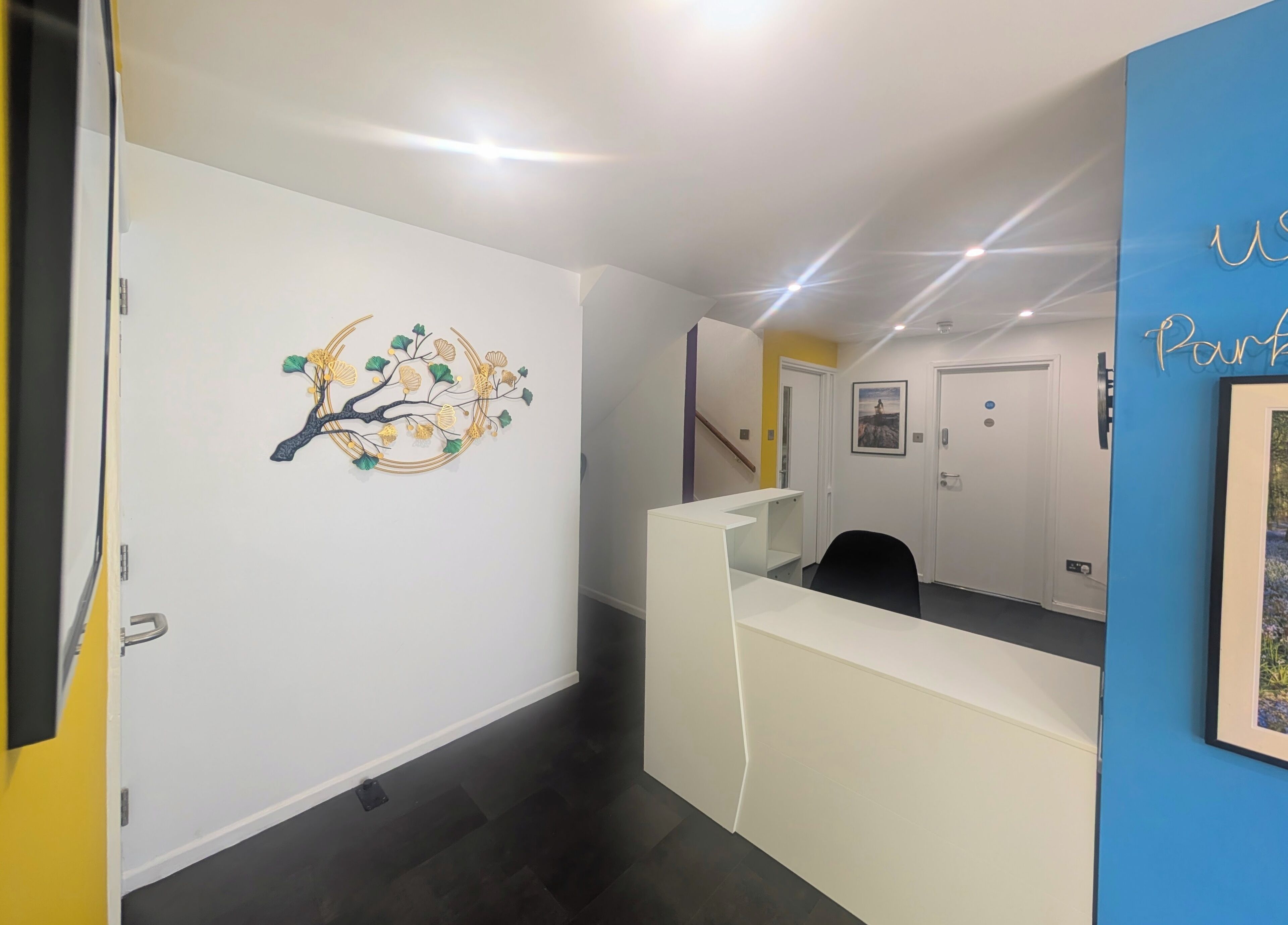 A reception area with a white desk, a wall-mounted artwork of a tree, and a blue wall with a nameplate.