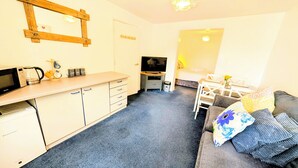 Un espacio habitable compacto con kitchenette, televisor, comedor y sofá.