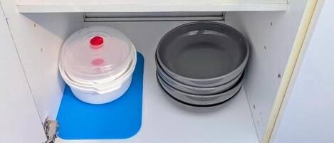 A kitchen with a white countertop, clear glass jars, a blue cutting board, and a stack of gray plates.