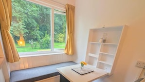 Una habitación con ventana, un banco, un escritorio, una silla y un pequeño cubo de basura.