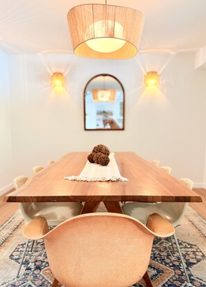 A dining room with a wooden table, chairs, a hanging light fixture, and wall sconces.