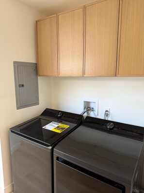 A laundry room with two stainless steel washers, wooden cabinets above, and a grey electrical panel on the wall. - 4-bedroom bungalow in welcoming Gardena with AC comfort (Gardena)