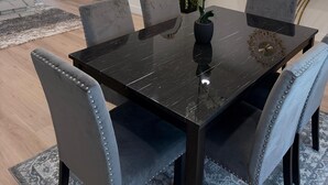 Et spiseområde med et sort bord, grå polstrede stole, en dekorativ lampe, et vægmonteret tv og et dekorativt ur.