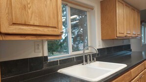 Una cocina con armarios de madera, encimera negra y ventana con vistas a árboles.