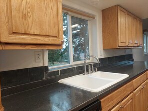 A kitchen with wooden cabinets, a black countertop, and a window with a view of trees.