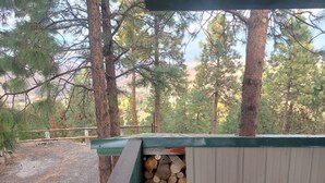 Un espacio al aire libre techado con piso de madera, una pila de leña y un cobertizo de metal.