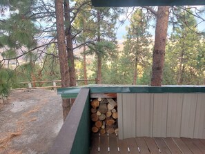 A covered outdoor area with a wooden deck, a stack of firewood, and a metal shed.