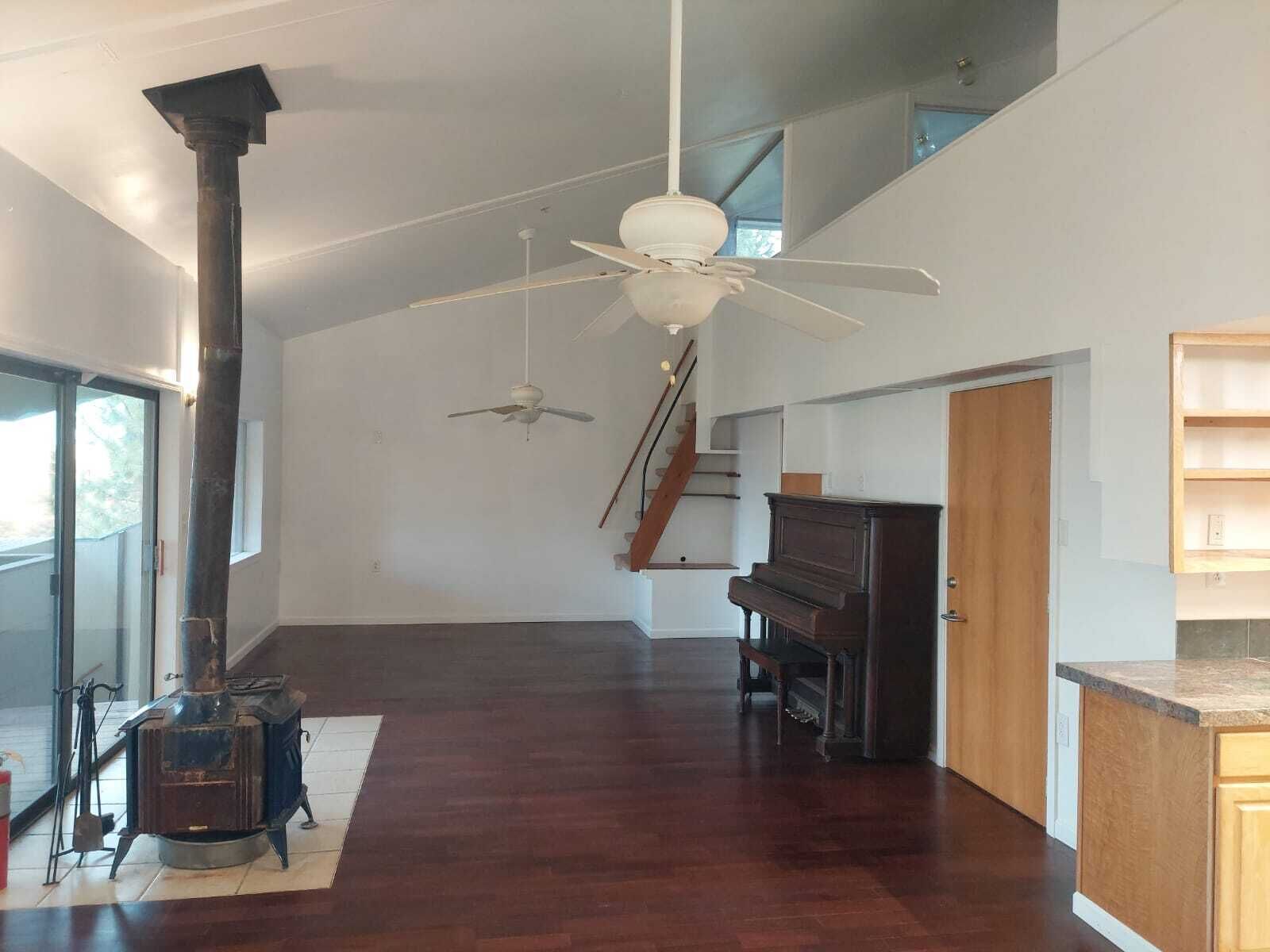Amplia habitación con suelo de madera, un piano, ventilador de techo y chimenea.