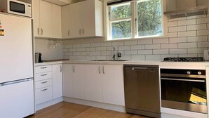 A modern kitchen with white cabinets, a dishwasher, a stove, and a window.