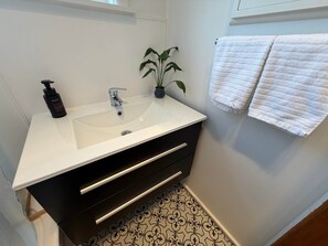 Un baño con lavamanos blanco, mueble negro y una planta en maceta.