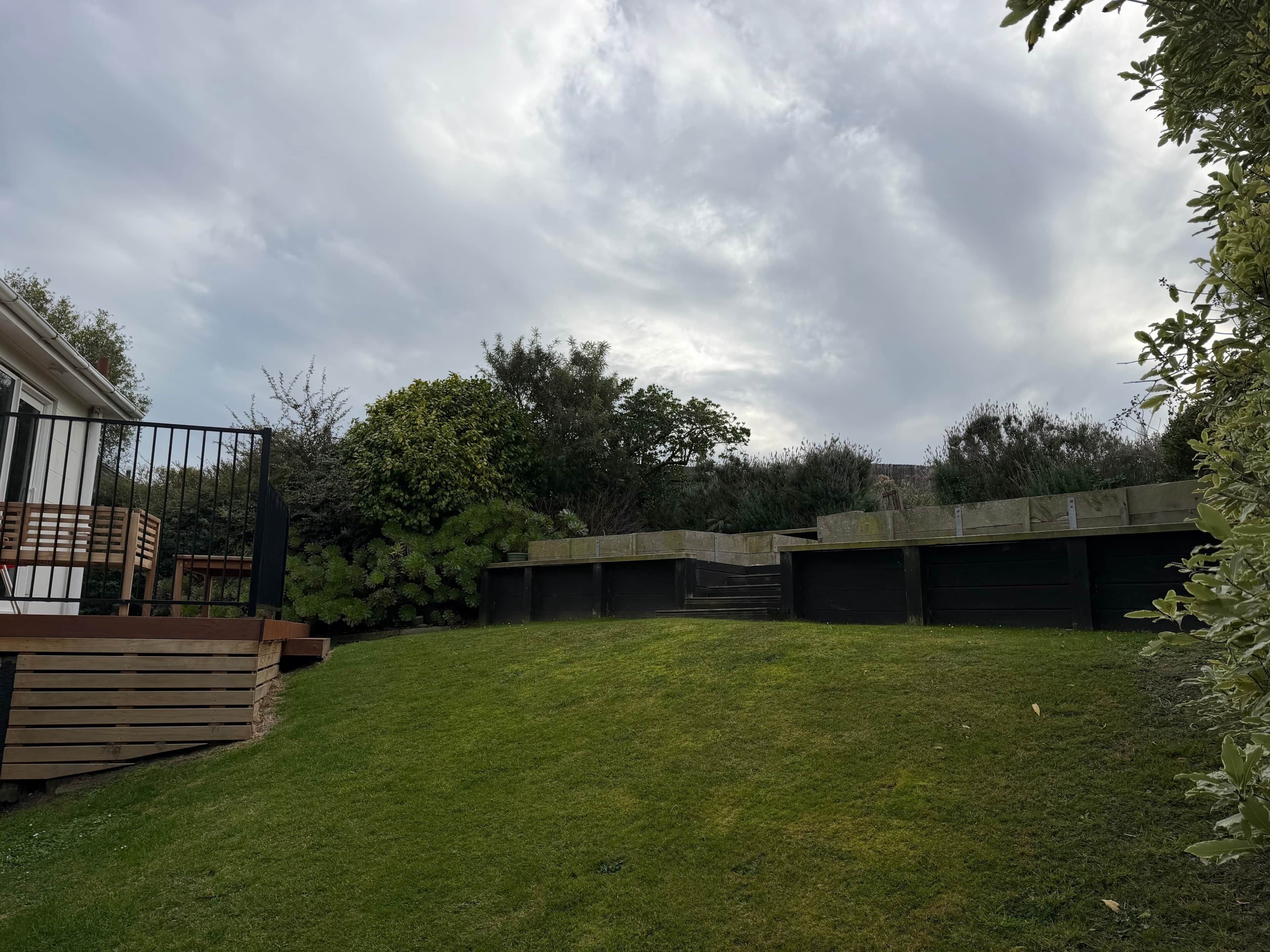 A backyard with a wooden deck, a grassy lawn, and a concrete structure.