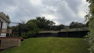 A backyard with a wooden deck, a grassy lawn, and a concrete structure.