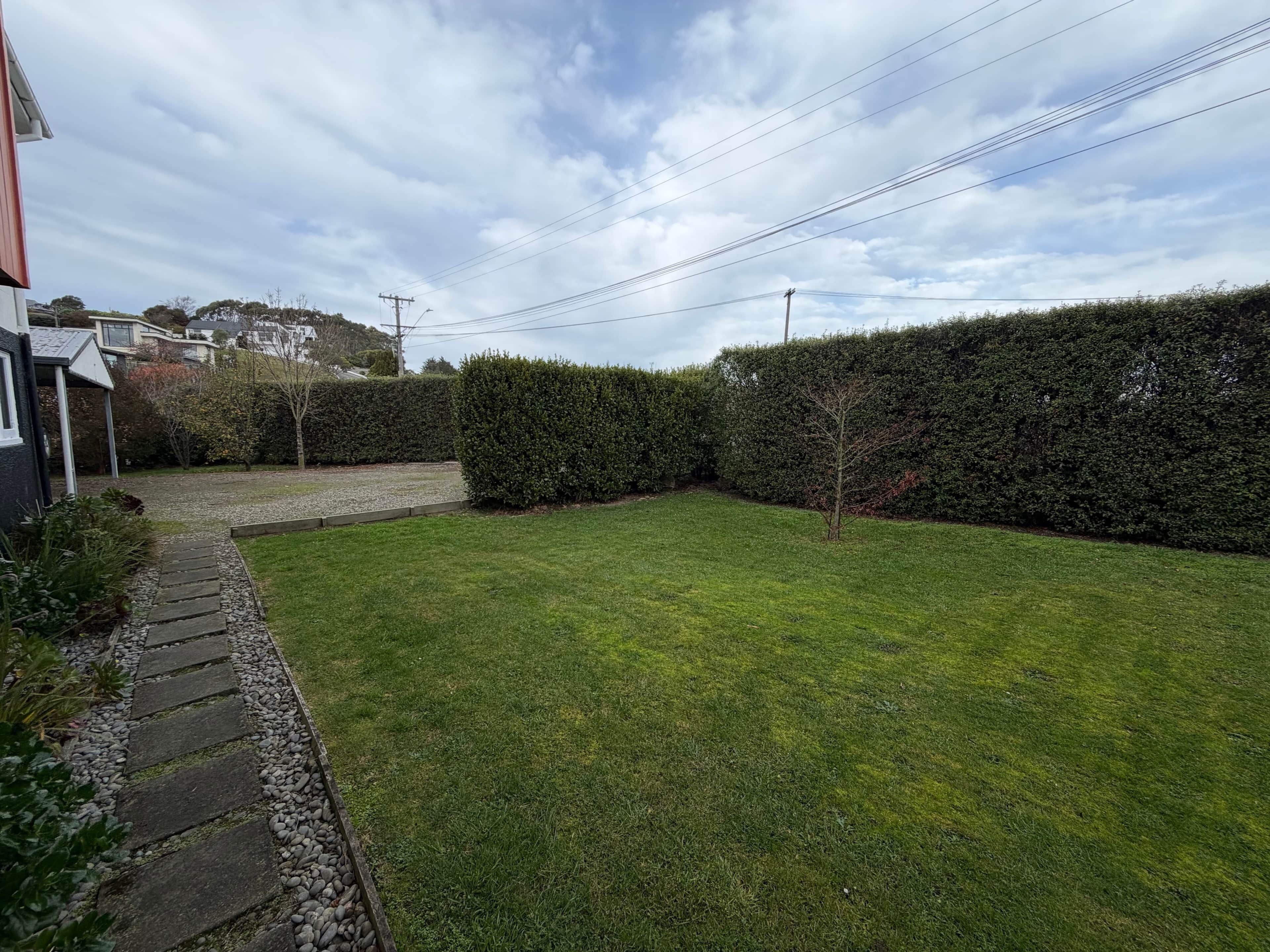 A residential backyard with a stone pathway, a hedge, and a grassy lawn.