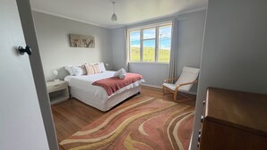 A bedroom with a bed, bedside table, lamp, chair, and a view of the outdoors.