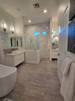 A modern bathroom with a bathtub, a glass-enclosed shower, and a vanity with a mirror. - Perfect golfers getaway! Palm Valley Oasis in Goodyear! (Goodyear)