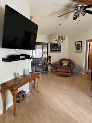 A living room with a flat-screen TV, wooden furniture, a ceiling fan, and a framed picture on the wall. - Beautiful 2-bedroom house with in convenient Spring Hill (Spring Hill)