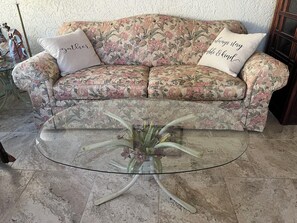 Un canapé à motifs floraux agrémenté de deux coussins, une table basse en verre et un vase rempli de fleurs.