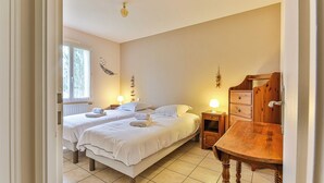 A bedroom with two beds, a wooden dresser, a nightstand, and a window with curtains.