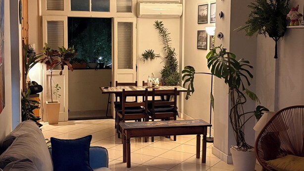 A living room with a sofa, coffee table, and a dining area with a table and chairs. - Suite in a shared apartment in Glória, Rio de Janeiro. (Rio de Janeiro)