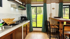 A kitchen with a wooden countertop, a sink, and a stove. There are wooden chairs and a table with a view of the outdoors.