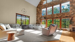 A spacious living room with a stone wall, large windows, a clock, and a fireplace. - Mountaintop Cabin|Game Room|Pickleball (Elliottsburg)