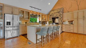 A modern kitchen with a stone accent wall, stainless steel appliances, and a bar area with stools. - Mountaintop Cabin|Game Room|Pickleball (Elliottsburg)