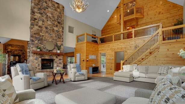 A spacious living area with a stone fireplace, leather sofas, and a wooden staircase. - Mountaintop Cabin|Game Room|Pickleball (Elliottsburg)