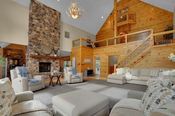 A spacious living area with a stone fireplace, leather sofas, and a wooden staircase.