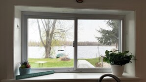 Une fenêtre donnant sur un lac, un quai avec un bateau, et une plante en pot posée sur le rebord de la fenêtre.