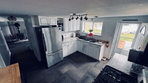Une cuisine de taille réduite, équipée d’un réfrigérateur, d’une cuisinière, d’un évier et de meubles blancs.
