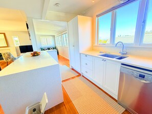 A modern kitchen with a central island, a built-in dishwasher, and a window providing natural light. - Parnell Gem | Walk to Domain & Hospital (Parnell)