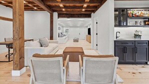 A modern interior with a wooden ceiling, white walls, a kitchen with dark cabinets, and a seating area with wicker chairs. - Capeside: 540-O Vintage Luxury in Orleans (Orleans)