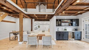 A spacious loft with a high ceiling, exposed wooden beams, a kitchen area, and a seating area with a sofa and chairs. - Capeside: 540-O Vintage Luxury in Orleans (Orleans)