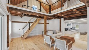 A spacious loft with exposed wooden beams, a staircase, a white sofa, and a dining area with chairs. - Capeside: 540-O Vintage Luxury in Orleans (Orleans)