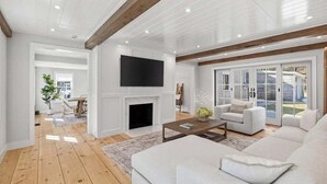A modern living room with a fireplace, white sofas, a flat-screen TV, and a large sliding glass door leading to an outdoor area. - Capeside: 540-O Vintage Luxury in Orleans (Orleans)
