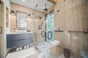 A modern bathroom with a wooden panel wall, a large mirror, a white sink, and a glass shower enclosure.