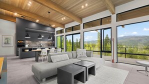 Un salon moderne avec un canapé d’angle, deux tables basses noires et une vue sur l’extérieur grâce à de grandes fenêtres.