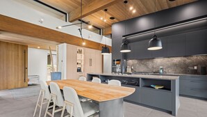 Une cuisine moderne avec une table à manger en bois, des meubles de couleur grise et des luminaires suspendus.