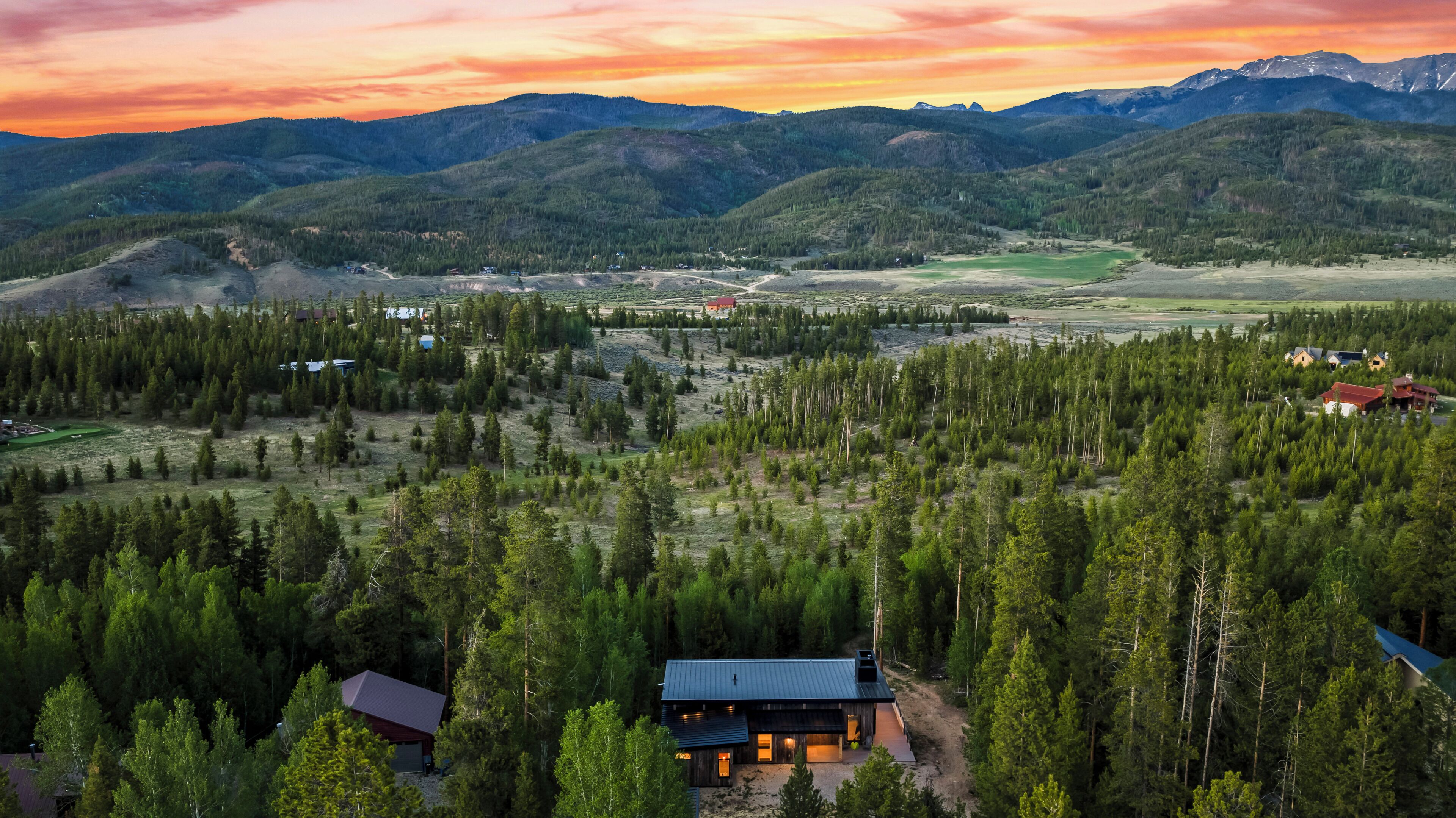 A remote cabin surrounded by dense forest, with a mountain range in the background.