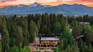 Une maison moderne entourée d’une forêt dense, avec une chaîne de montagnes en arrière-plan.