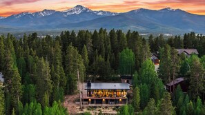 A modern house surrounded by dense forest with a mountain range in the background.