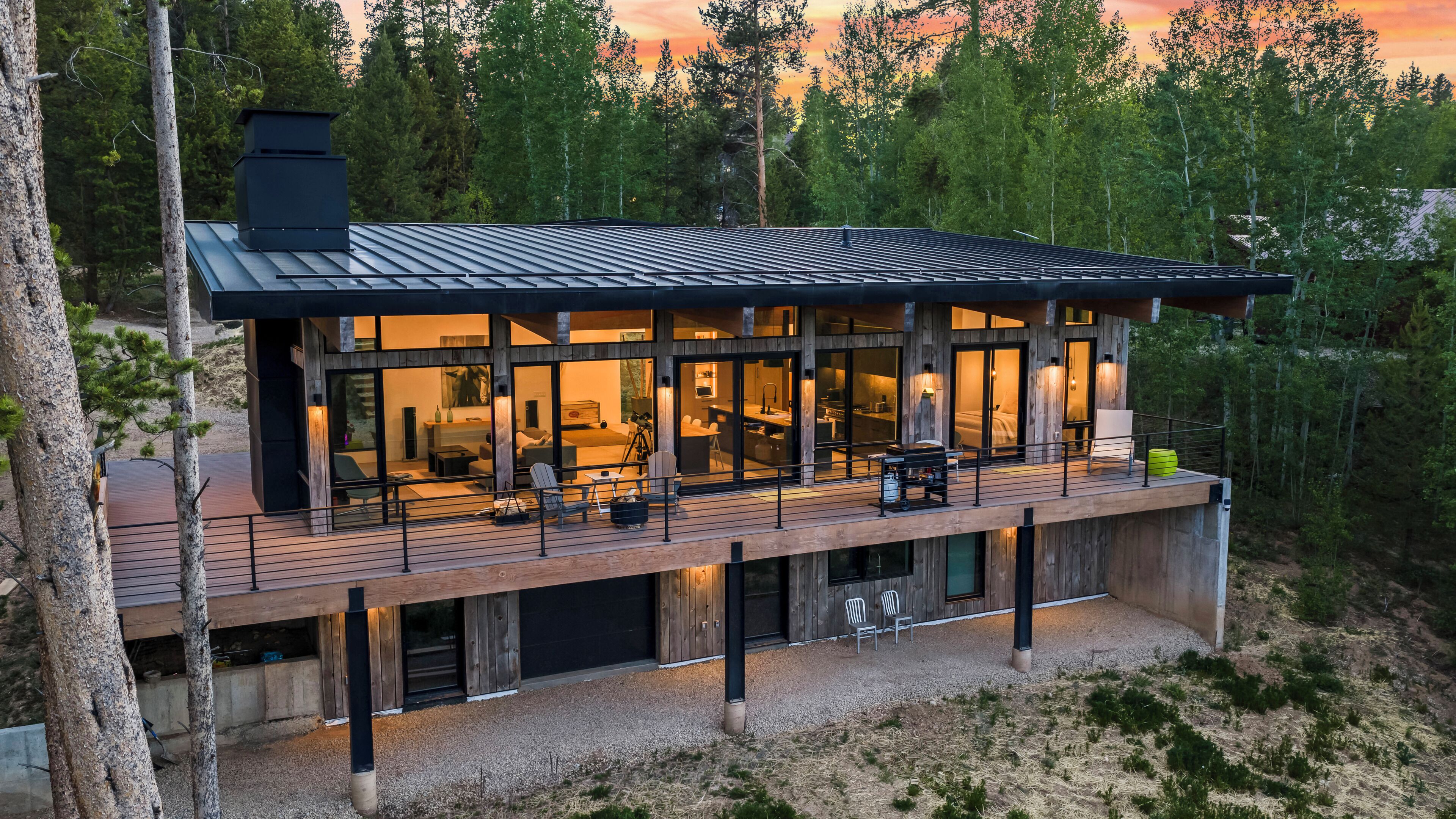 A modern house with a deck, large windows, and a view of the forest.