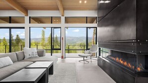 Un salon moderne doté d’une cheminée, de grandes fenêtres et offrant une vue sur les montagnes.