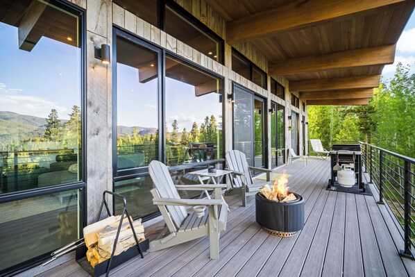 A deck with Adirondack chairs, a fire pit, and a grill.